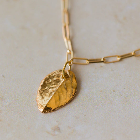 gold leaf charm bracelet with paperclip chain resting on soft stone surface, handcrafted nature-inspired jewellery by Iris & Lolli