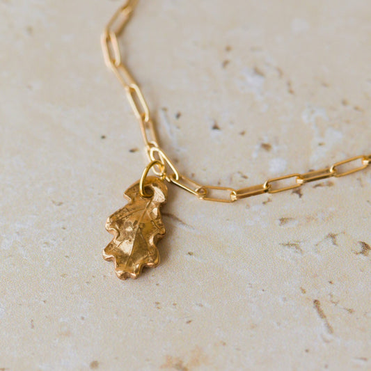 gold oak leaf charm bracelet with paperclip chain styled flat on neutral stone background, nature-inspired jewellery by Iris & Lolli