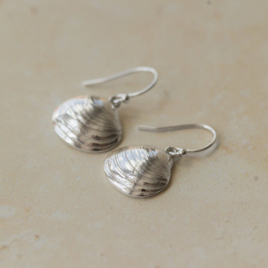 Close-up of handmade recycled silver Shell earrings by Iris and Lolli on a neutral background, showing delicate clam shell texture and natural ocean-inspired detail