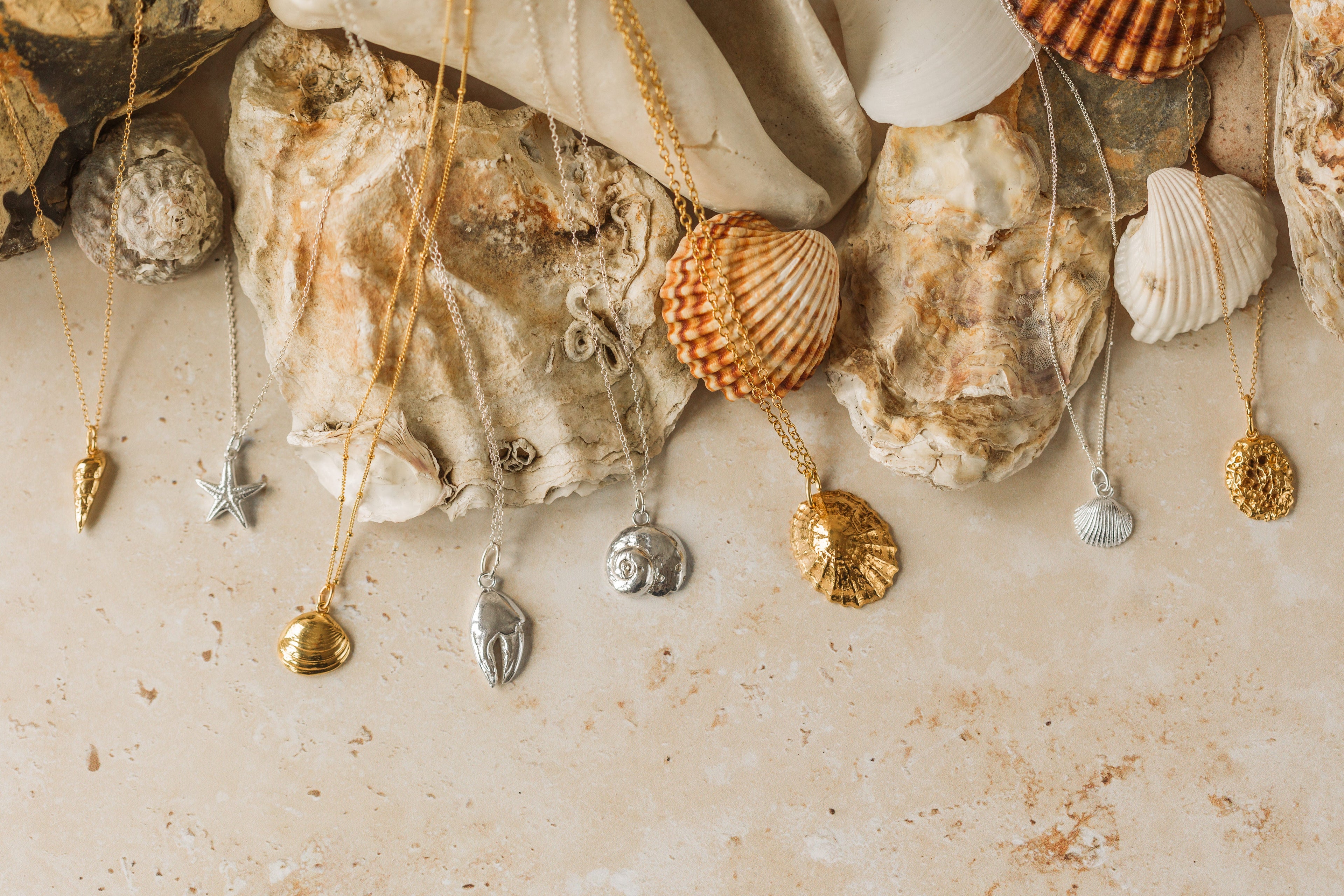 Gold and silver ocean-inspired necklaces displayed with natural shells and stones – handcrafted jewellery from Iris & Lolli