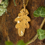 Gold leaf pendant necklace on a wooden surface with green leaves
