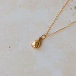 Gold necklace with a small bell pendant on a light beige background