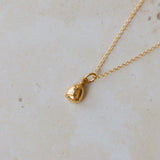 Gold necklace with a small bell pendant on a light beige background