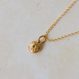 Gold necklace with a small round pendant on a light beige background