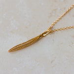 Gold necklace with a leaf pendant on a light beige surface