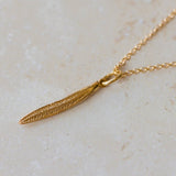 Gold necklace with a leaf pendant on a light beige surface