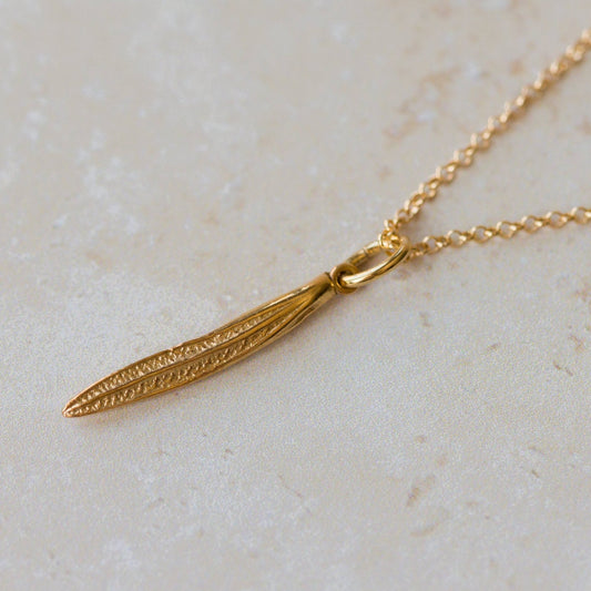 Gold necklace with a leaf pendant on a light beige surface
