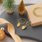 Gold earrings on a dark surface with decorative items including a small Christmas tree and ribbon.