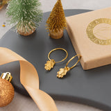 Gold earrings on a dark surface with decorative items including a small Christmas tree and ribbon.