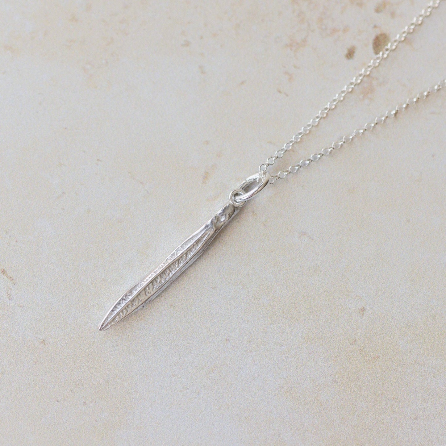 Silver necklace with a pendant on a light beige marble surface