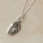 Silver crab claw pendant on a chain against a beige background