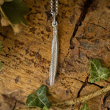 Silver leaf pendant necklace on a wooden surface with green leaves.