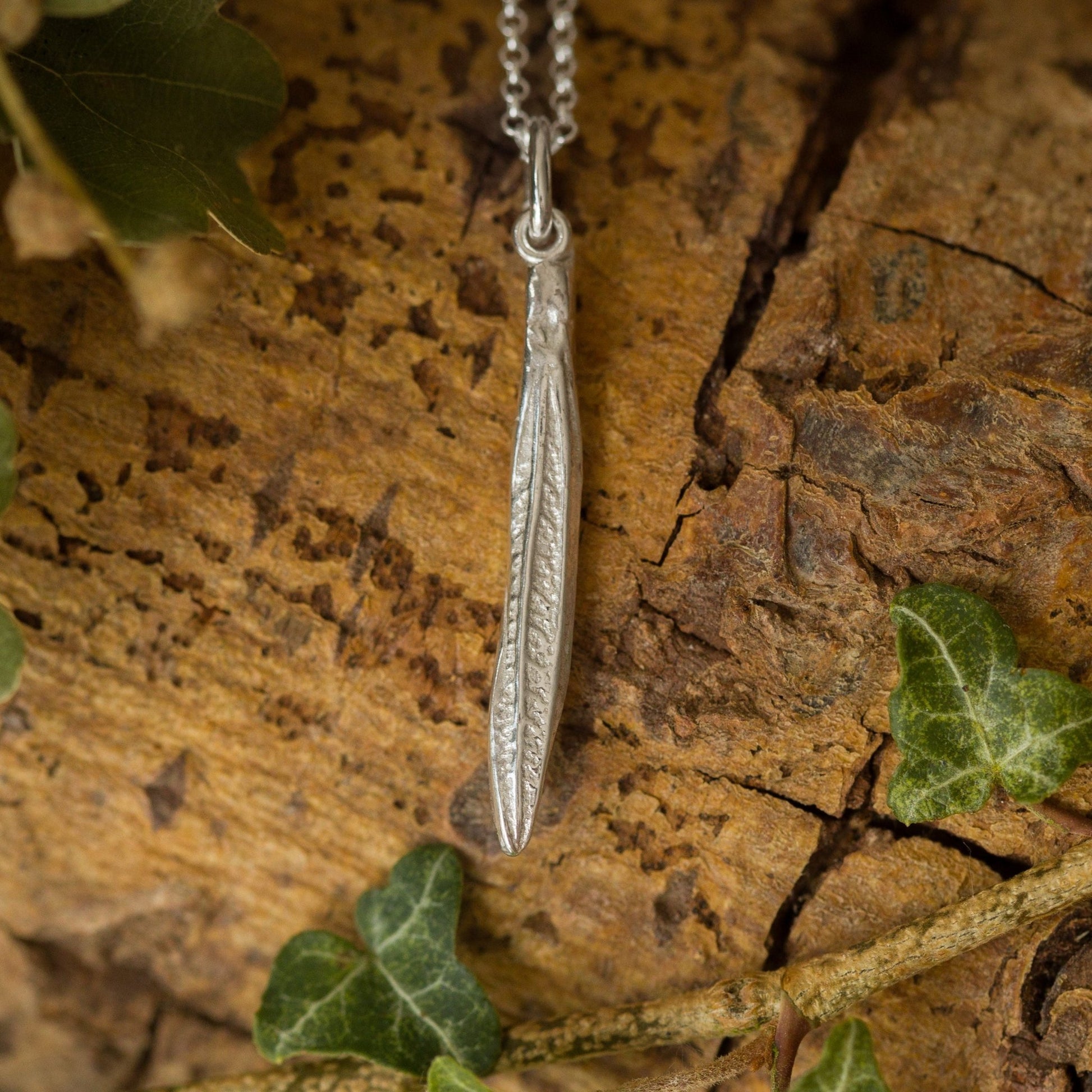 Silver leaf pendant necklace on a wooden surface with green leaves.