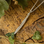 Silver necklace on a textured wooden surface with leaves