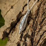 Silver pendant on a chain hanging on a textured wooden surface with green leaves.