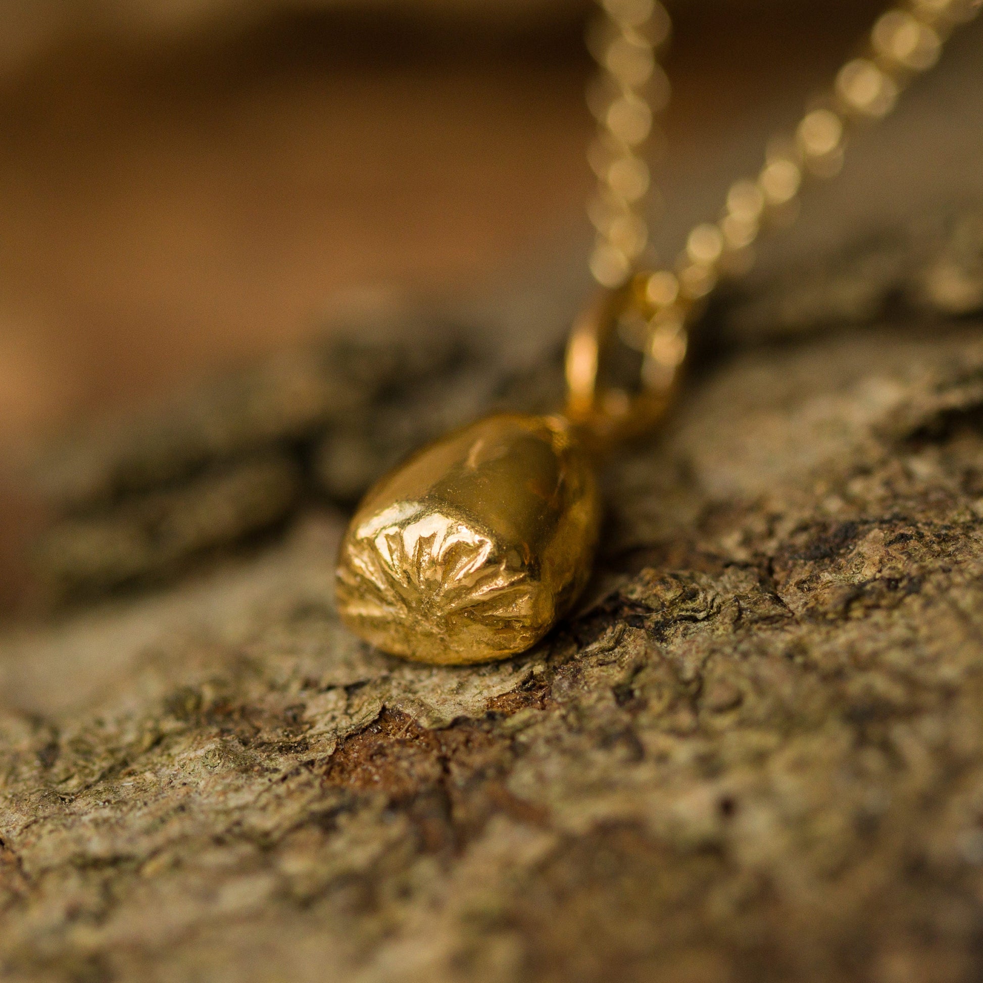 Gold pendant on a chain lying on textured stone surface