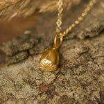 Gold necklace with a pendant on a stone surface with dried grasses