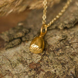 Gold necklace with a pendant on a stone surface with dried grasses