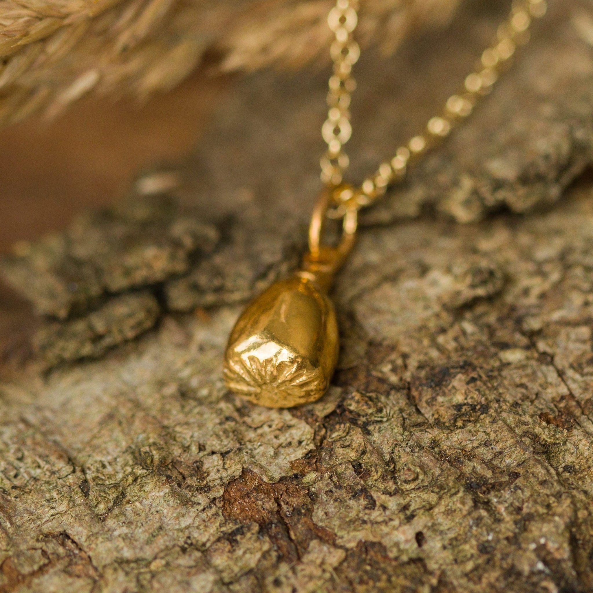 Gold necklace with a pendant on a stone surface with dried grasses