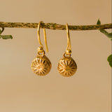 Gold earrings with sunflower design on a beige background