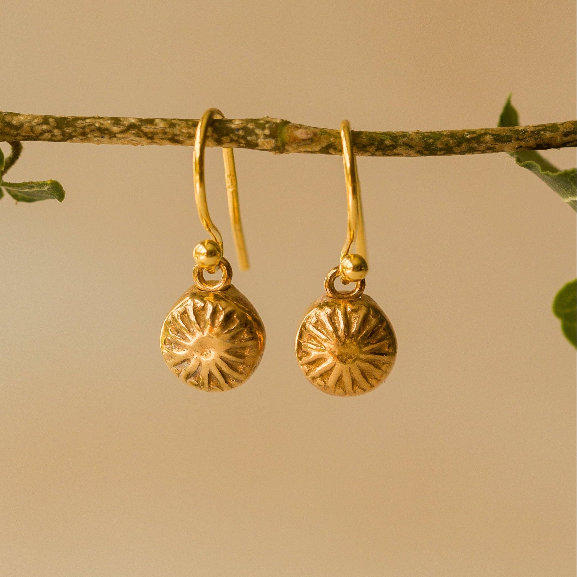Gold earrings with sunflower design on a beige background
