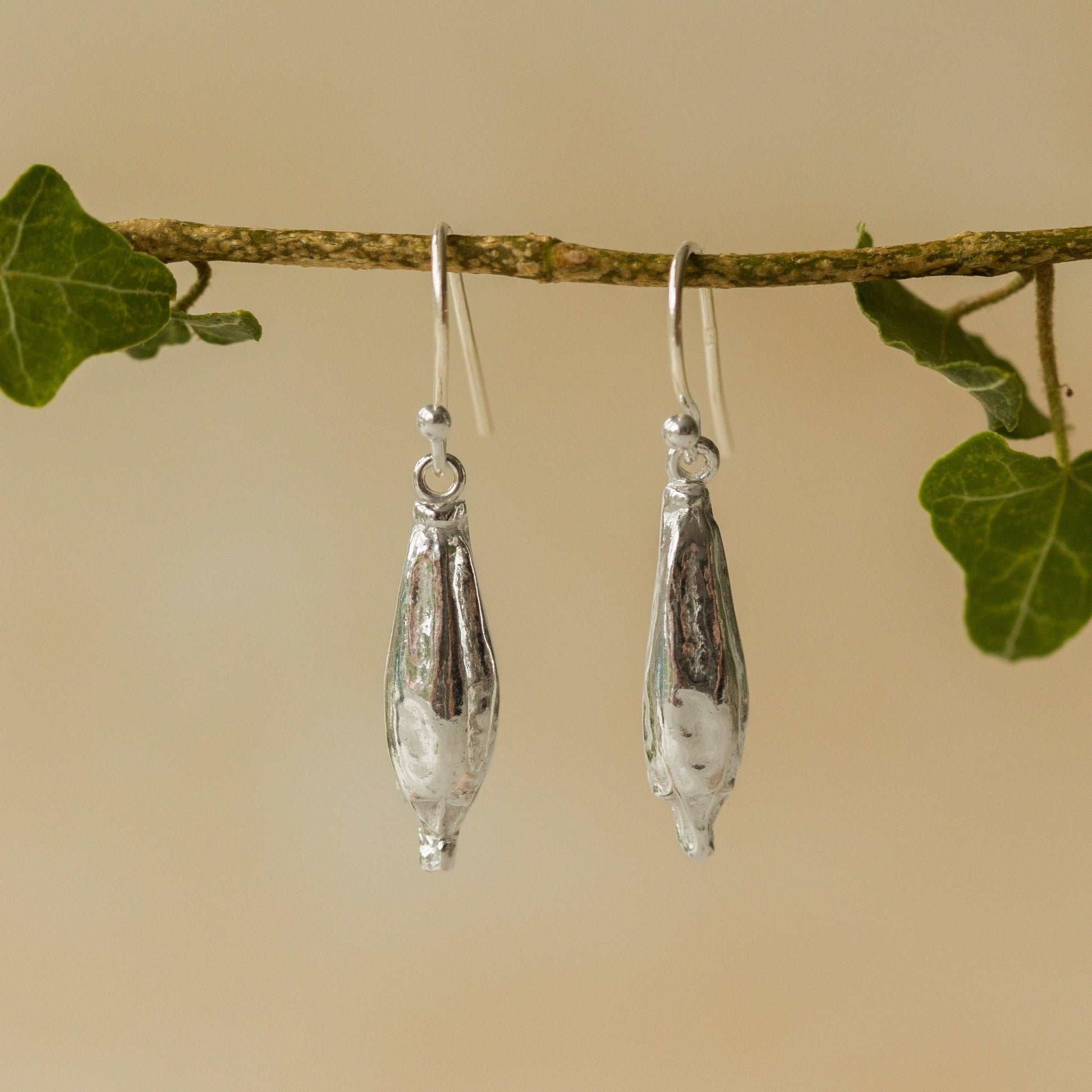 Silver teardrop earrings hanging from a branch with green leaves.