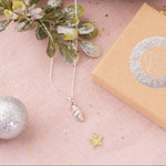 Flatlay of gold oak leaf necklace and silver acorn necklace displayed on driftwood with festive decorations and Iris & Lolli gift box, nature-inspired Christmas jewellery.