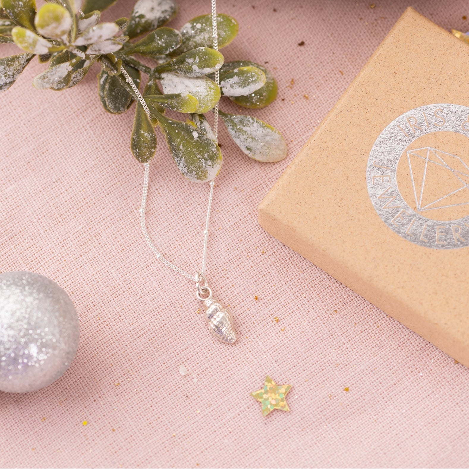 Flatlay of gold oak leaf necklace and silver acorn necklace displayed on driftwood with festive decorations and Iris & Lolli gift box, nature-inspired Christmas jewellery.