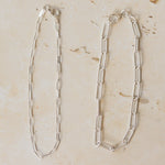 three fine silver chain bracelets displayed on neutral stone background, featuring delicate trace chain, medium link chain and paperclip chain designs