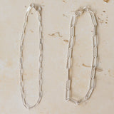 three fine silver chain bracelets displayed on neutral stone background, featuring delicate trace chain, medium link chain and paperclip chain designs