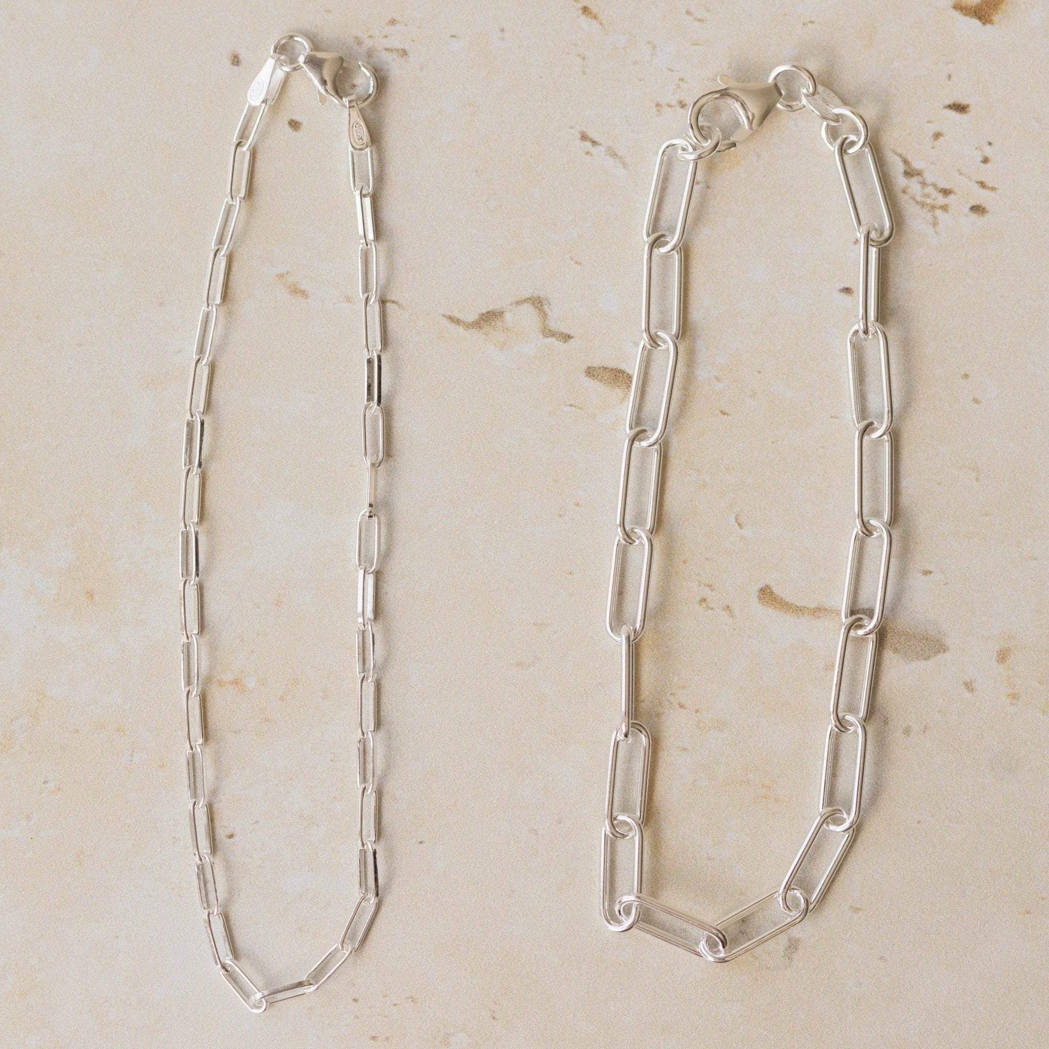 three fine silver chain bracelets displayed on neutral stone background, featuring delicate trace chain, medium link chain and paperclip chain designs