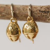 close up of gold acorn drop earrings with textured finish, handcrafted nature inspired jewellery displayed on wooden twig