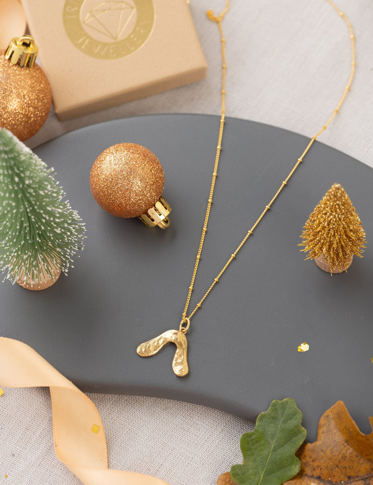 Gold baby sycamore necklace on a slate dish with Christmas baubles