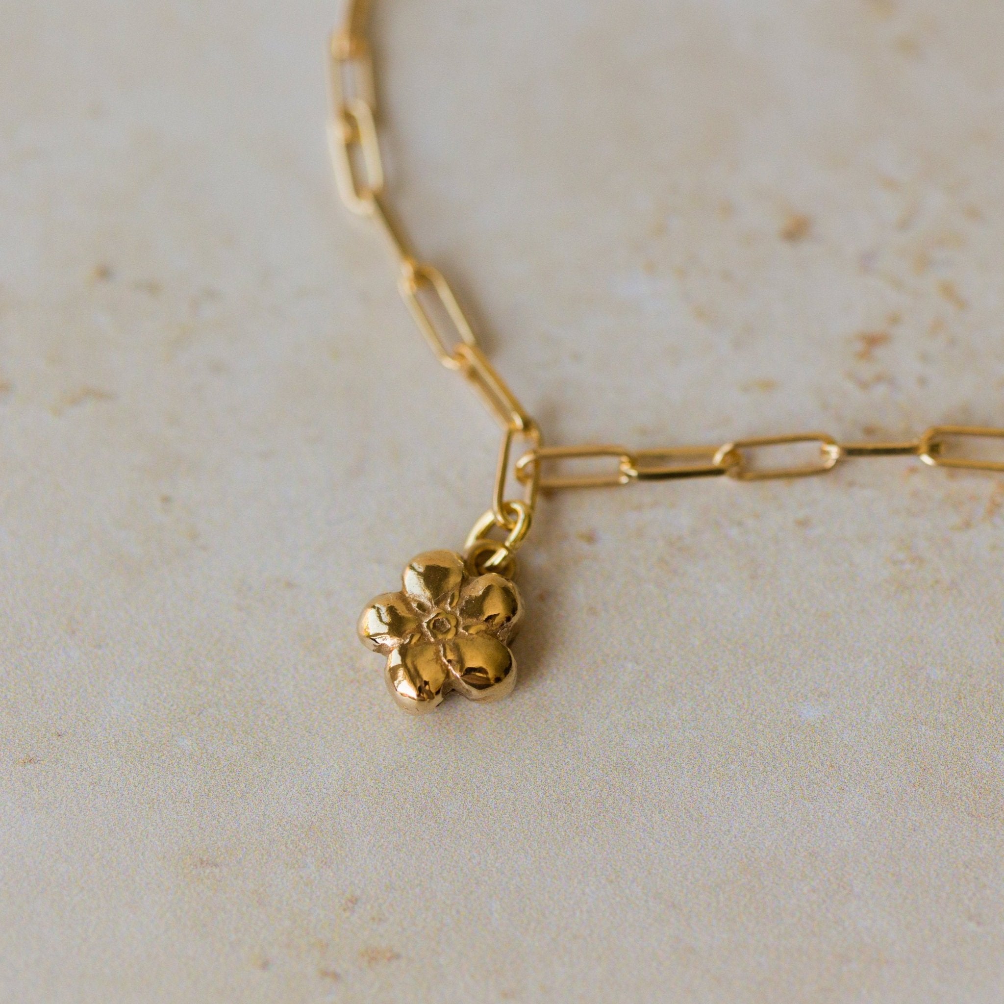 gold flower charm bracelet with paperclip chain resting on neutral stone surface, handcrafted floral jewellery by Iris & Lolli