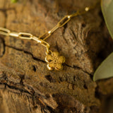 gold flower charm bracelet with paperclip chain displayed on natural wood surface, handcrafted botanical jewellery by Iris & Lolli