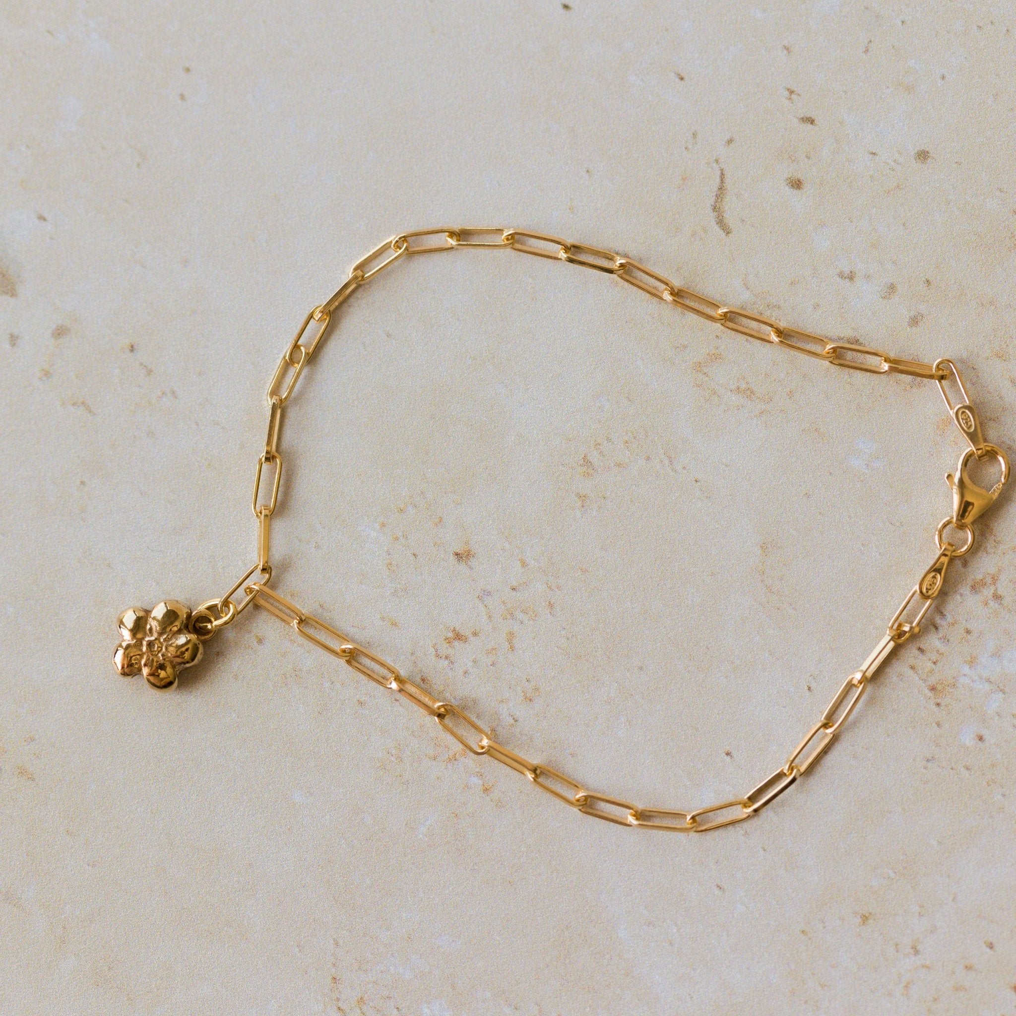 gold forget me not flower charm bracelet with paperclip chain styled flat on neutral stone surface, handcrafted floral bracelet by Iris & Lolli