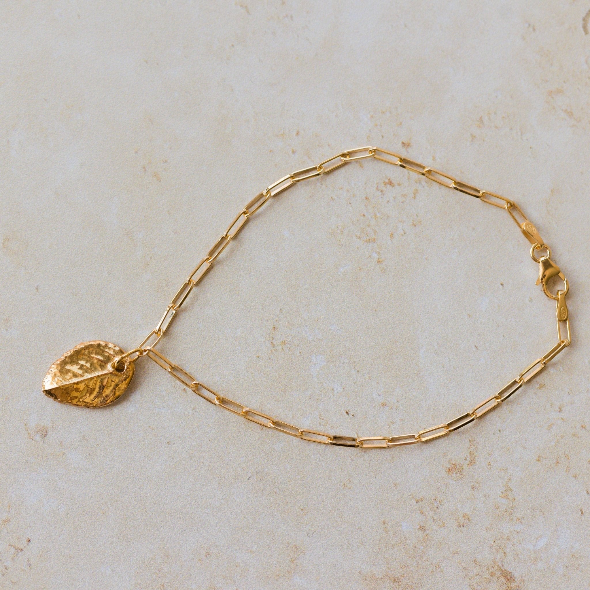 gold leaf charm bracelet with paperclip chain displayed on neutral stone background, handmade gold jewellery by Iris & Lolli