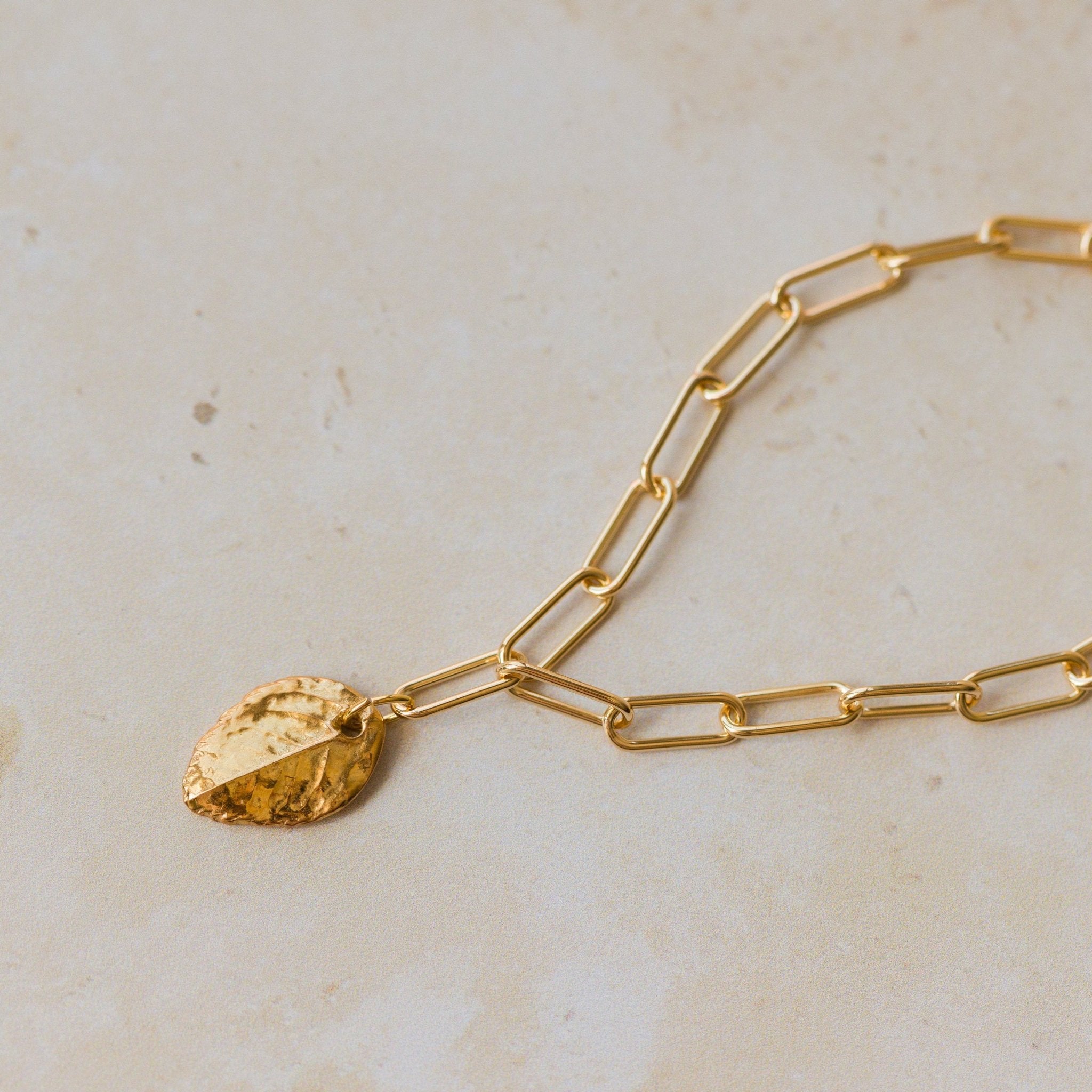 close up of gold leaf charm bracelet with paperclip chain on neutral background, handmade botanical jewellery by Iris & Lolli