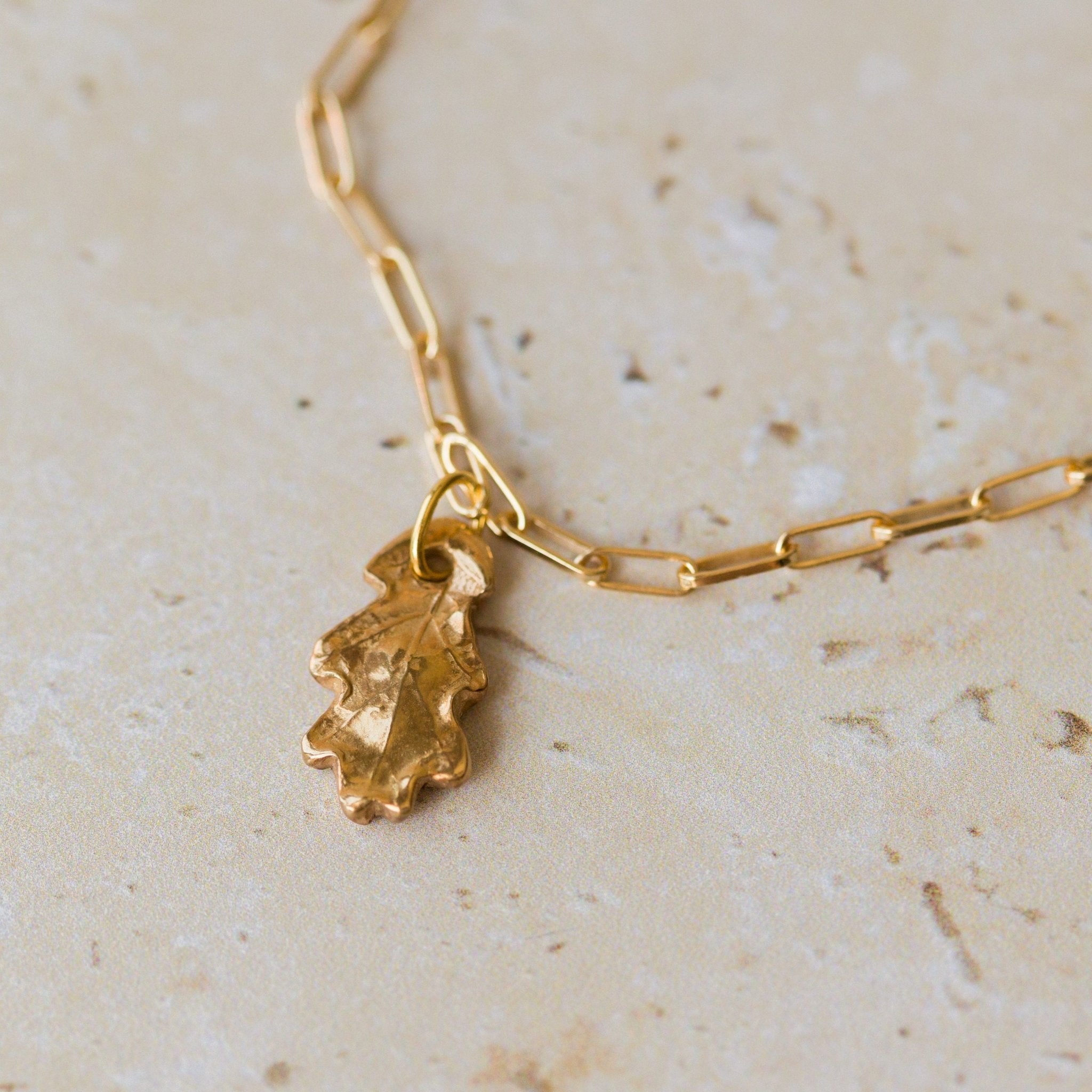 gold oak leaf charm bracelet with paperclip chain styled flat on neutral stone background, nature-inspired jewellery by Iris & Lolli