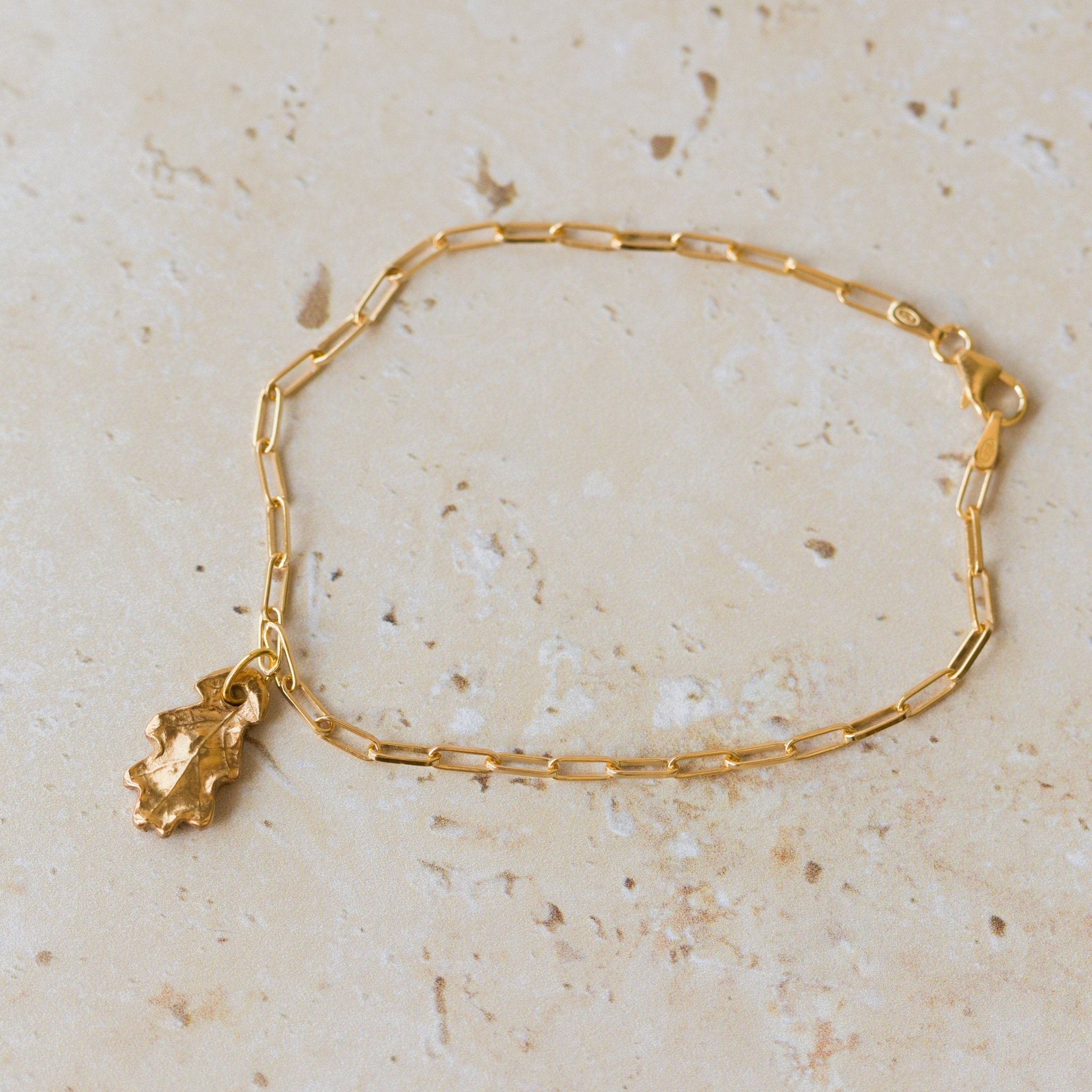 gold oak leaf charm bracelet with delicate paperclip chain styled on neutral stone surface, handcrafted woodland-inspired jewellery by Iris & Lolli