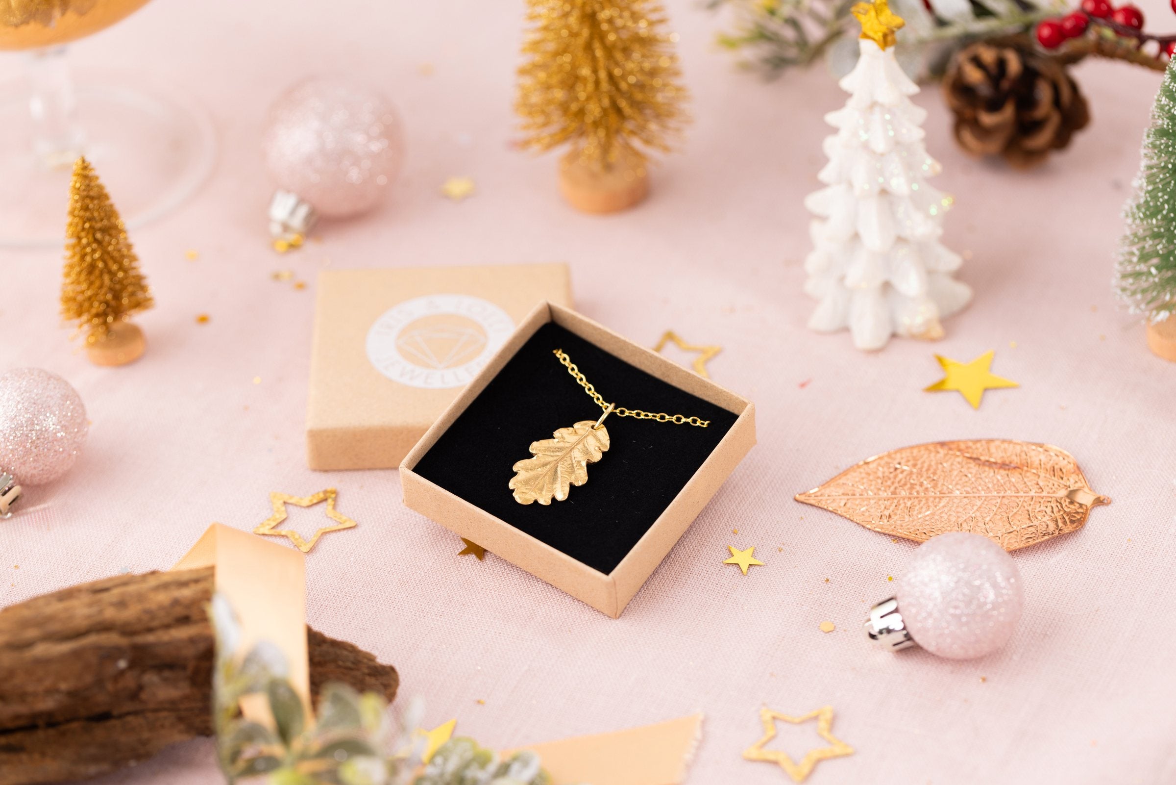 Gold oak leaf necklace in an Iris & Lolli gift box, surrounded by Christmas baubles and trees