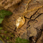 gold rose leaf charm bracelet resting on bark with ivy and dried grasses, botanical inspired handmade jewellery by Iris & Lolli
