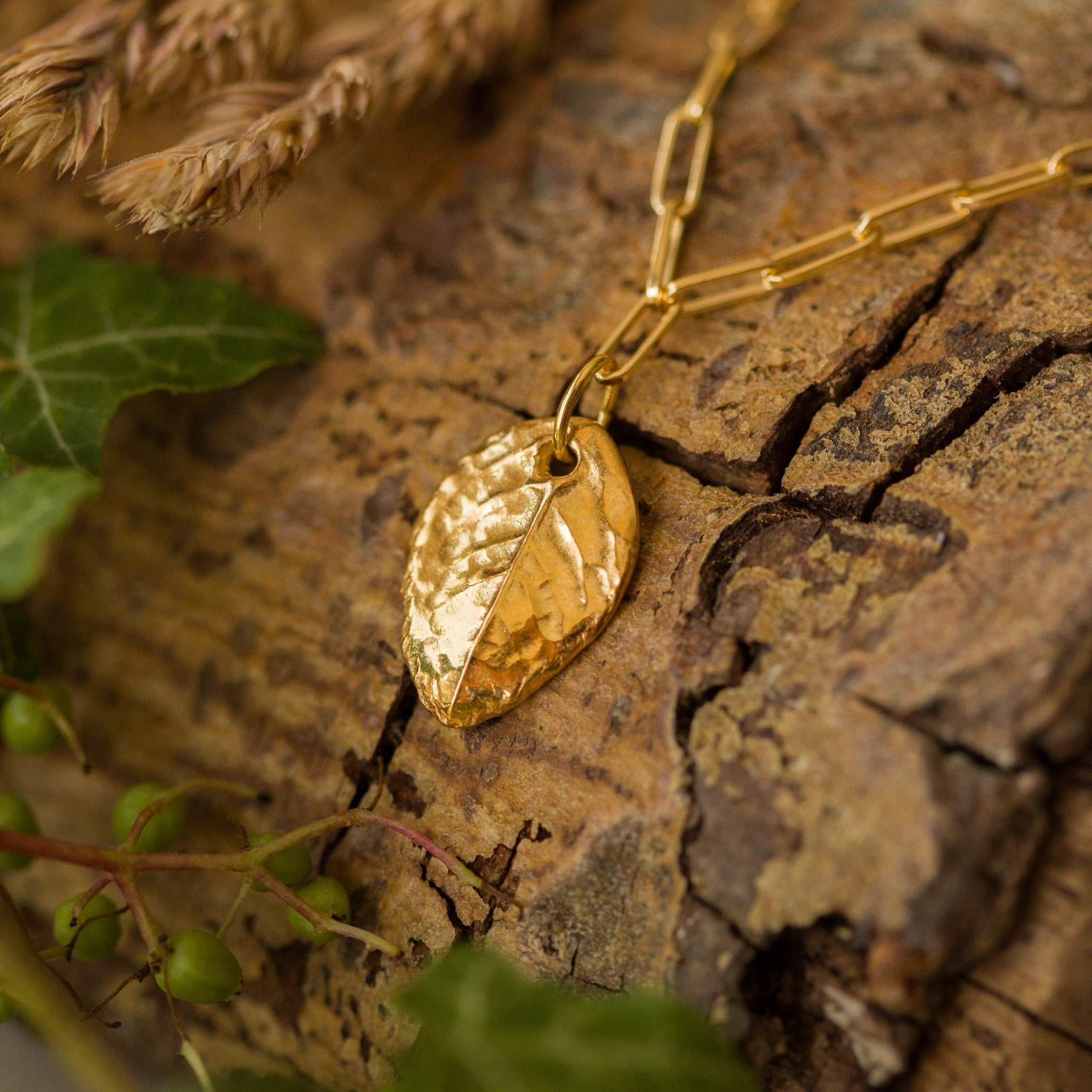 gold rose leaf charm bracelet resting on bark with ivy and dried grasses, botanical inspired handmade jewellery by Iris & Lolli
