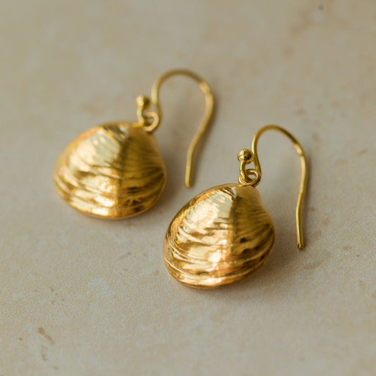 Handmade recycled gold Venus Clam earrings by Iris and Lolli laid flat on a sandy background, showcasing organic shell texture and soft coastal-inspired shine