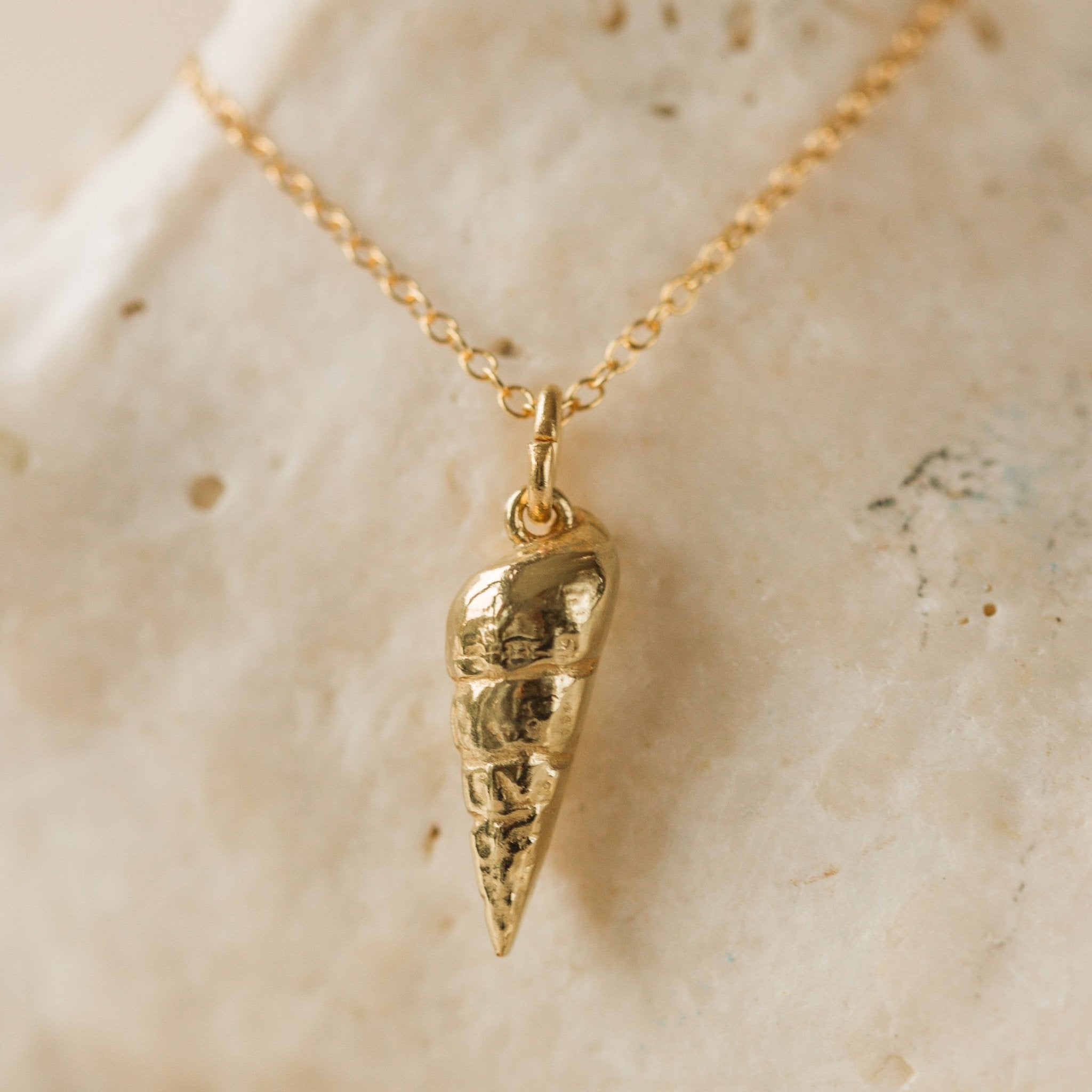 Gold shell necklace on a beige stone background
