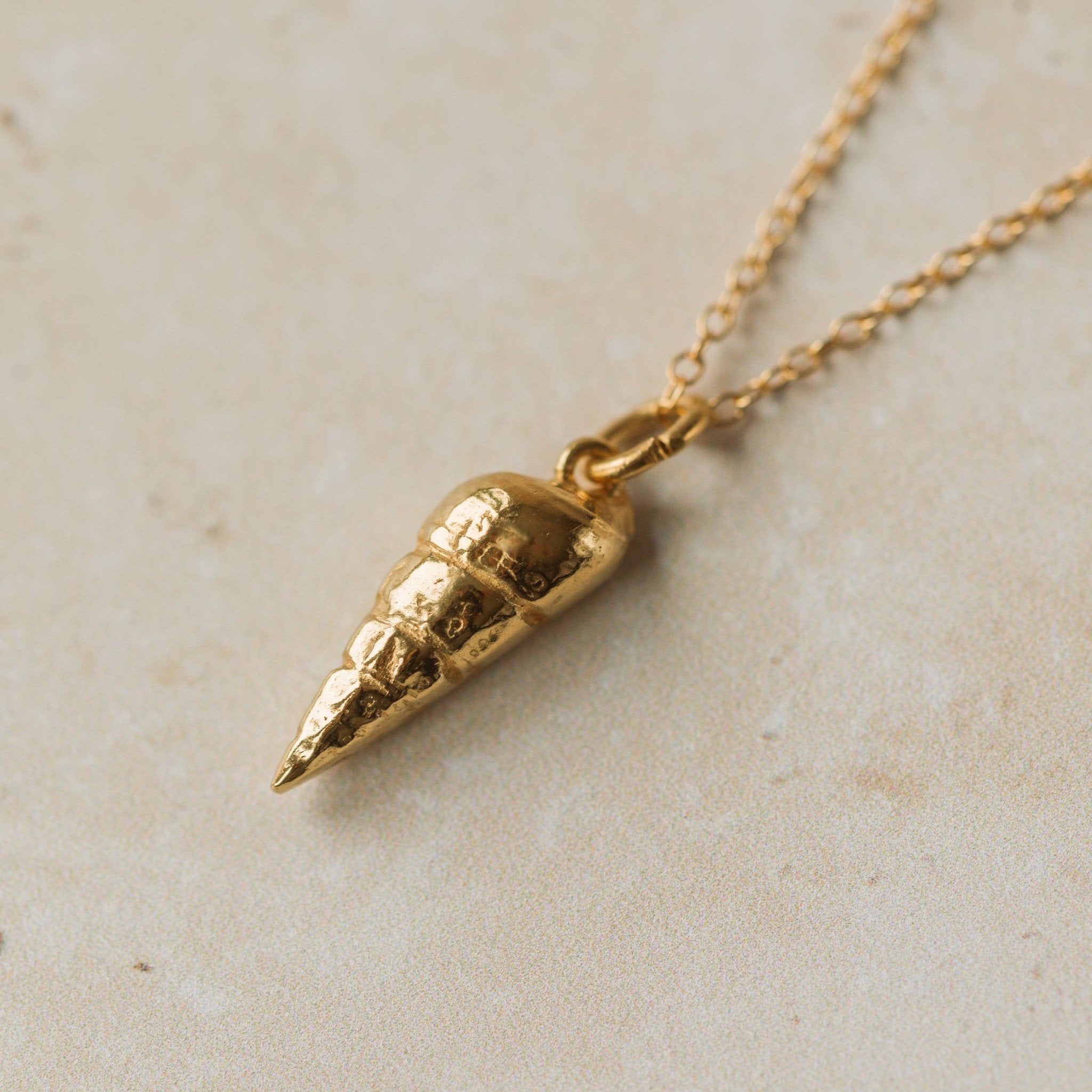 Gold shell pendant necklace on a light beige surface