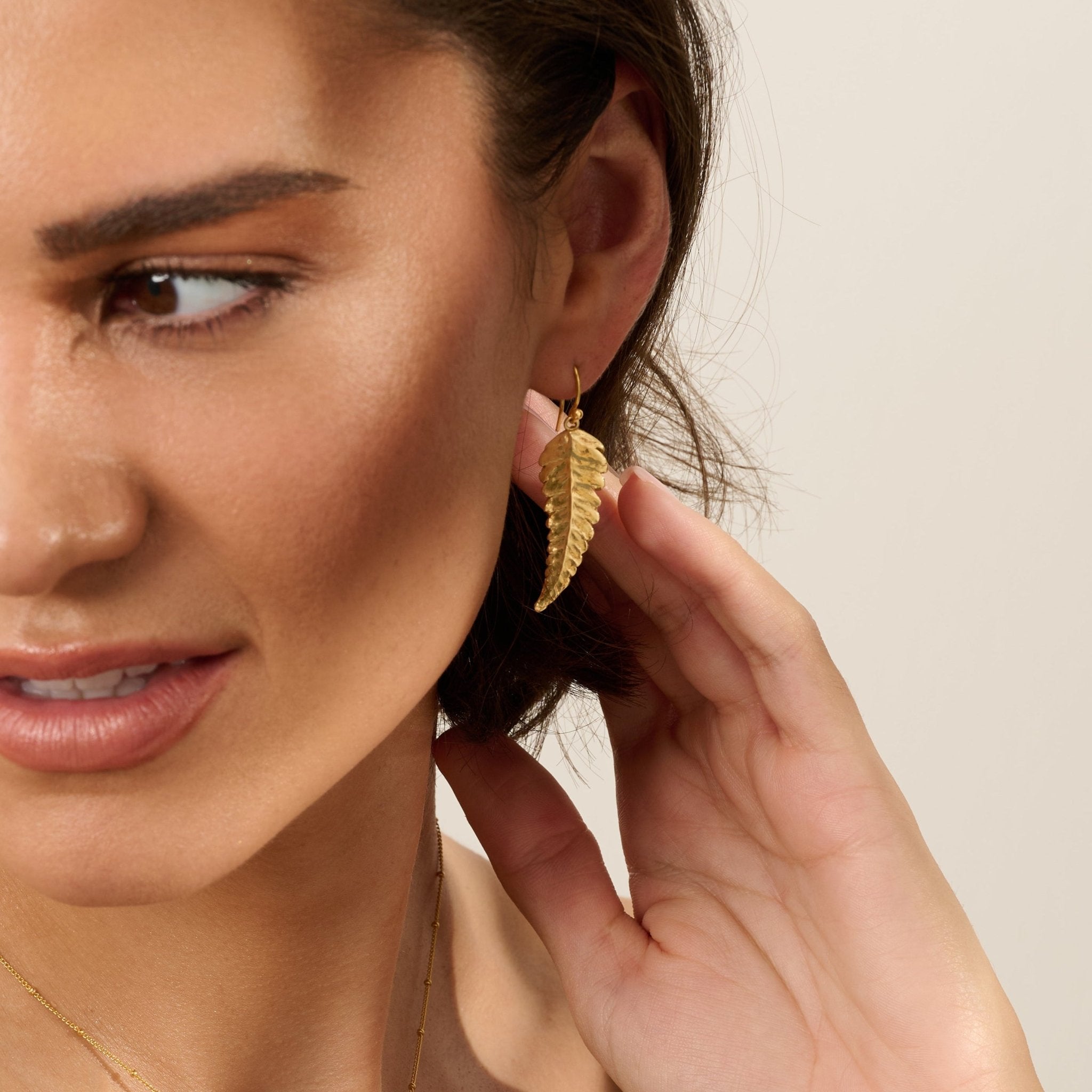 Model wearing handmade recycled gold fern leaf drop earring and necklace by Iris and Lolli, nature inspired and crafted in the UK
