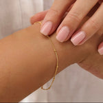 Gold satellite bracelet on a wrist with a neutral background