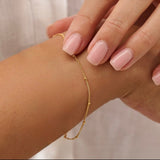 Gold satellite bracelet on a wrist with a neutral background