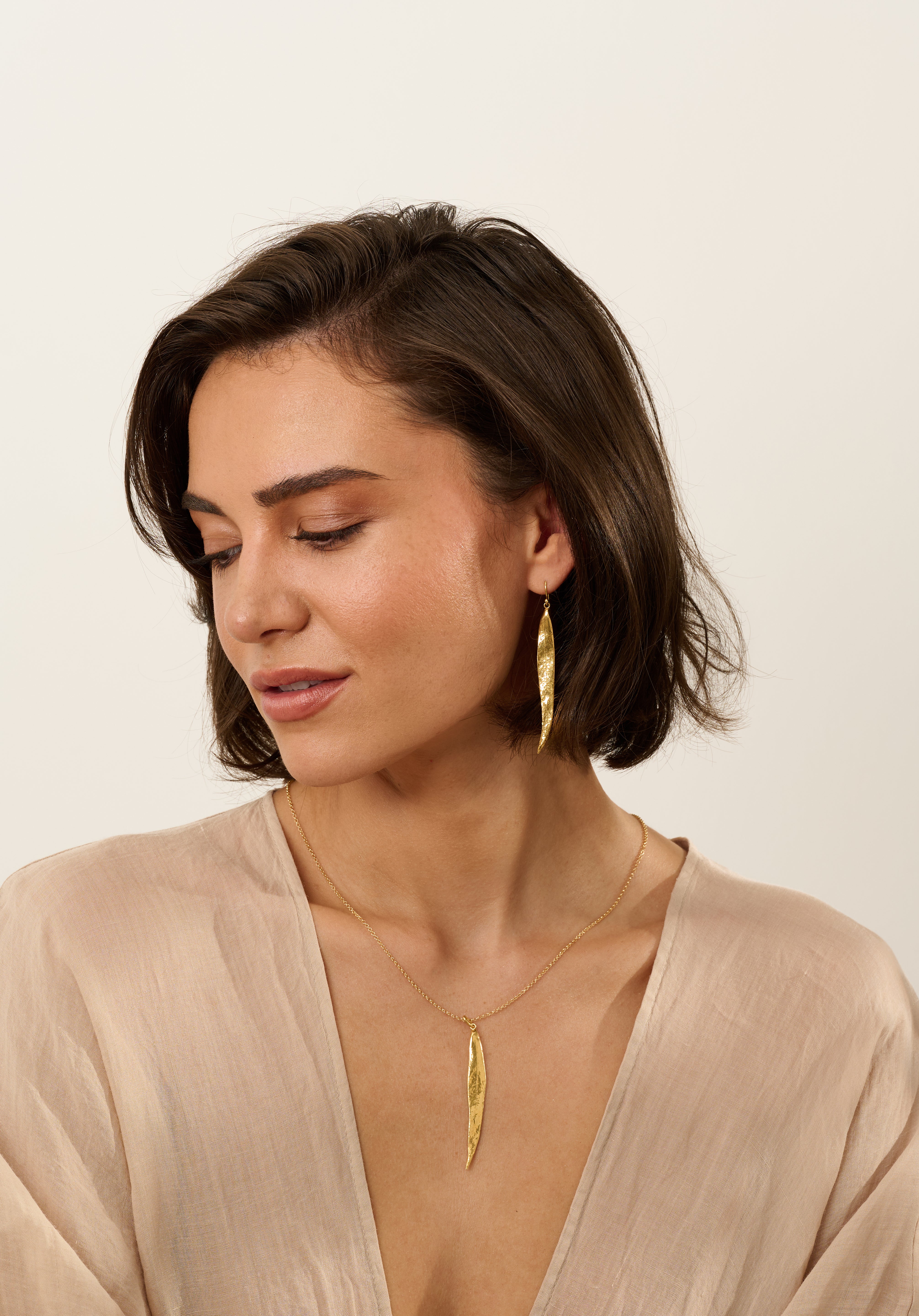 Model wearing matching gold willow leaf necklace and long gold willow leaf earrings, handcrafted botanical jewellery with organic textured leaf design.